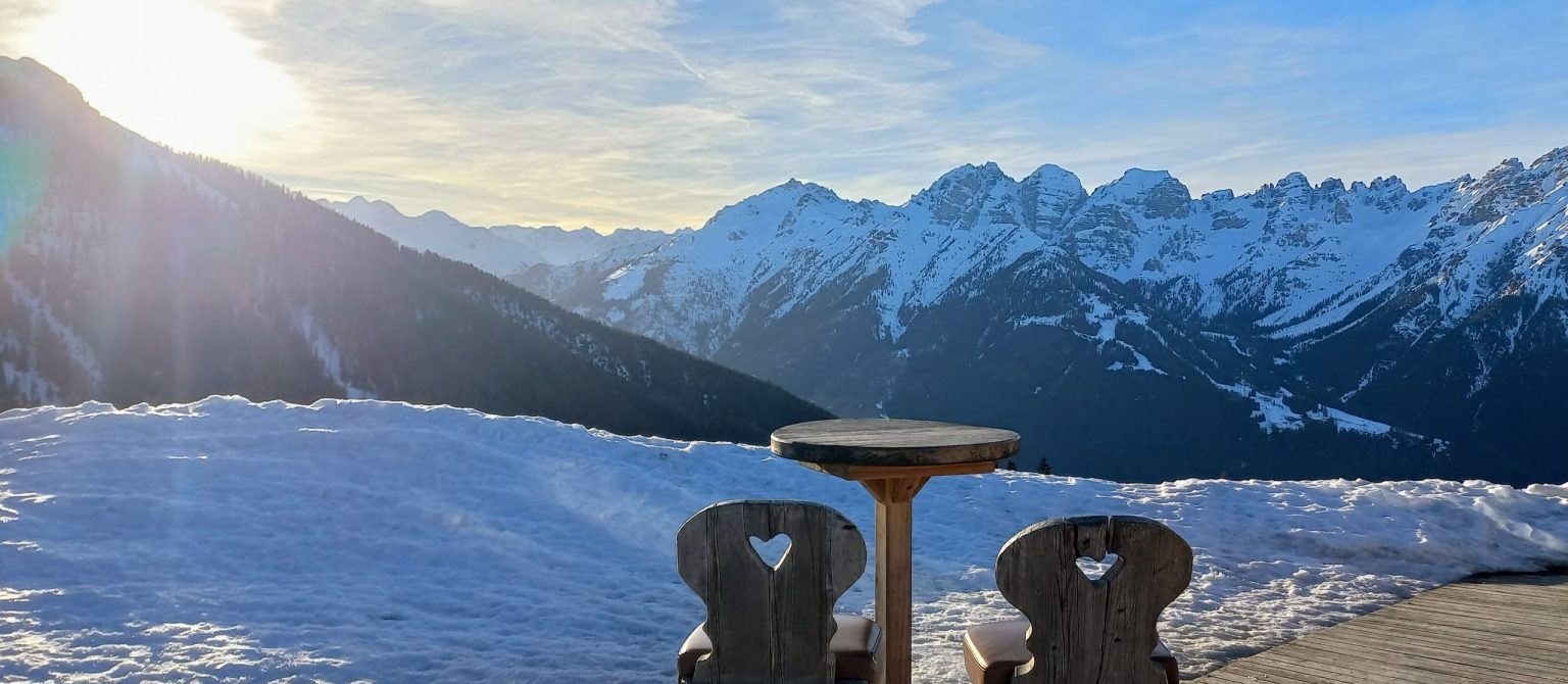 2 Stühle auf einer Holzterasse im Schnee mit Blick auf Berge in Sonnenuntergangsstimmung